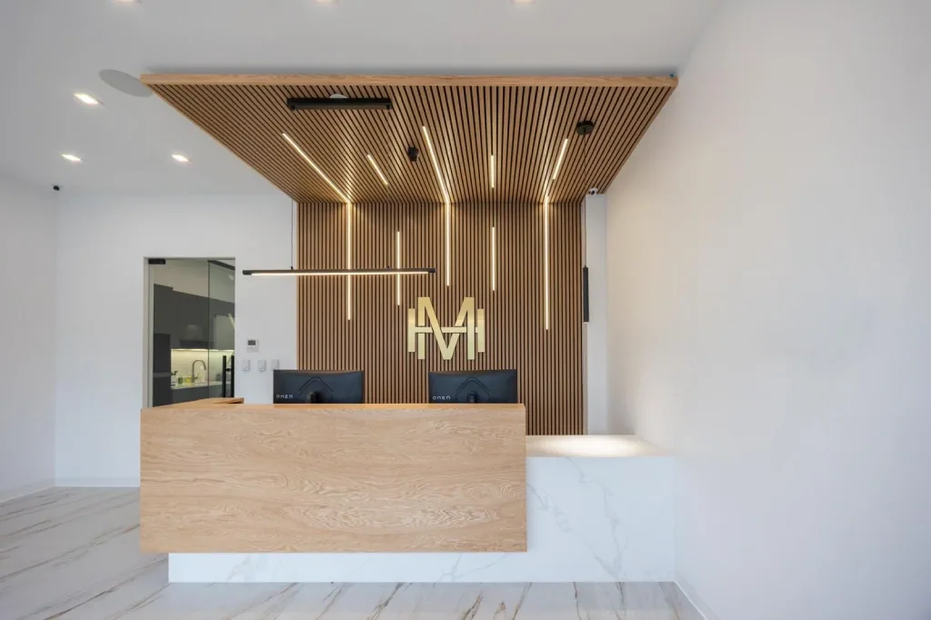 The reception of Modern Dental Hub: a wood-slat wall and ceiling with light strips, the gold monogram and the front desk