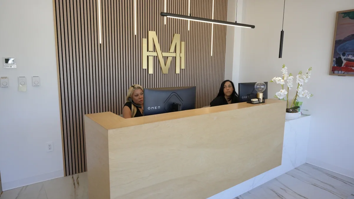 The reception desk at Modern Dental Hub with the gold monogram on a wood-slat wall