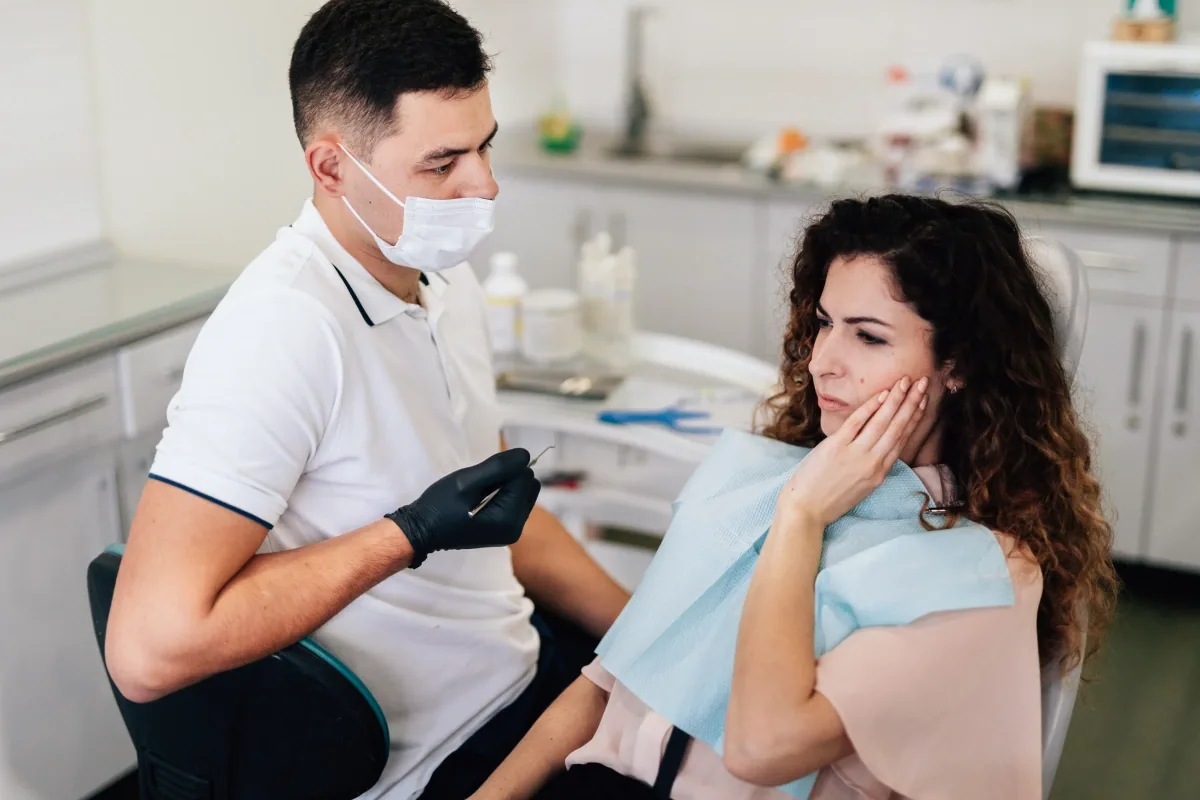 A patient holding her cheek in pain while a dentist listens (illustrative stock photo)