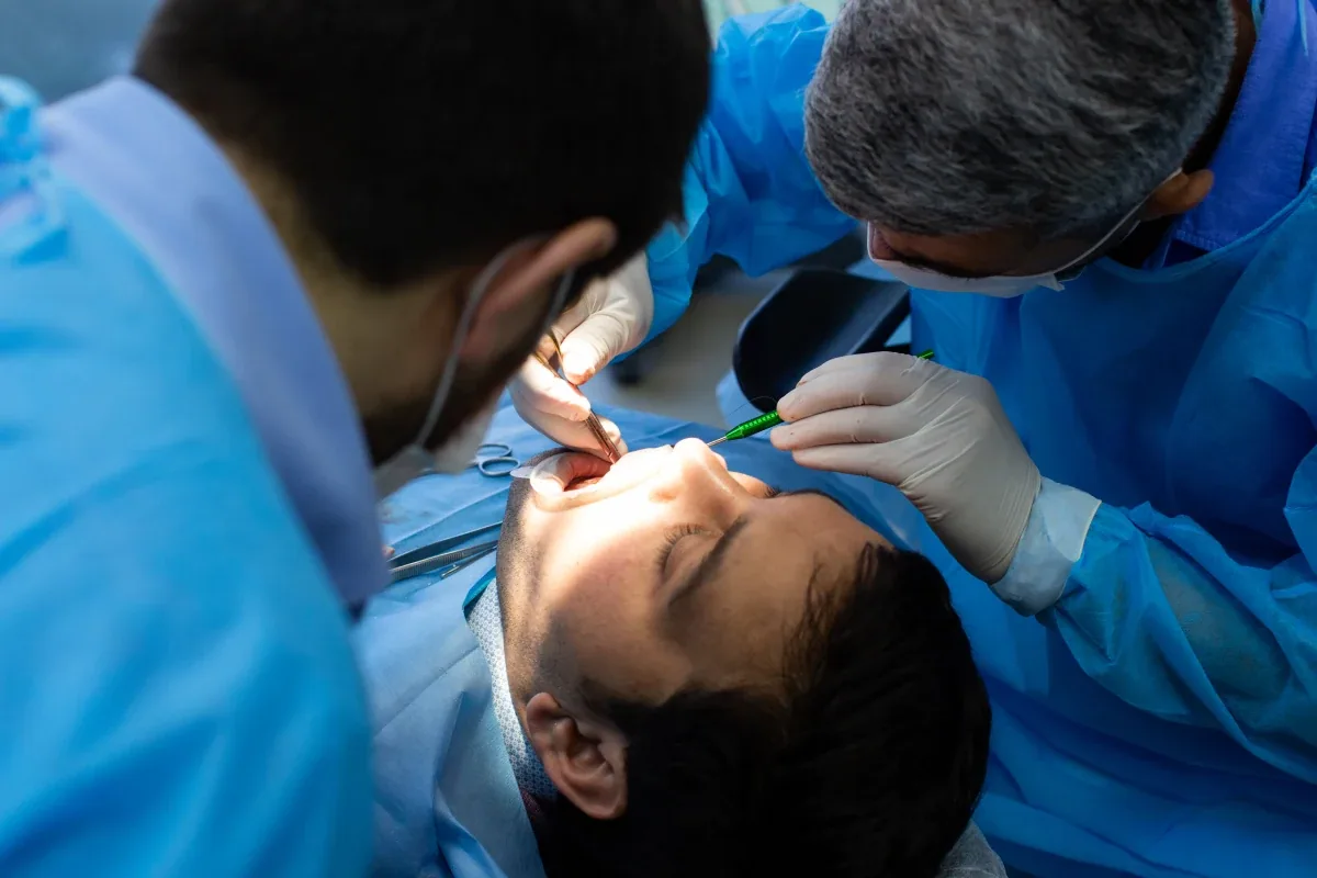 Two clinicians in surgical gowns performing an oral surgery procedure (illustrative stock photo)